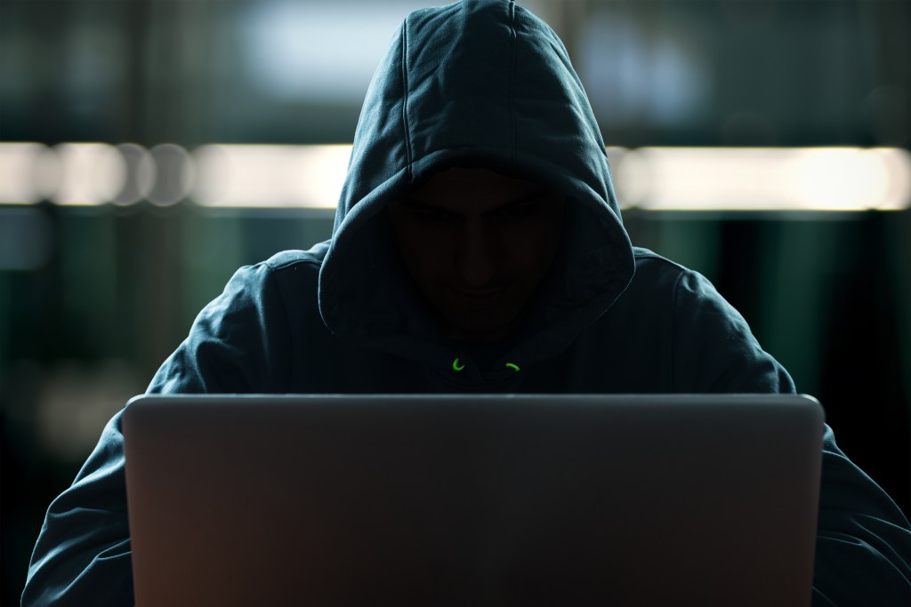 A shadowy figure in a hood on a computer.