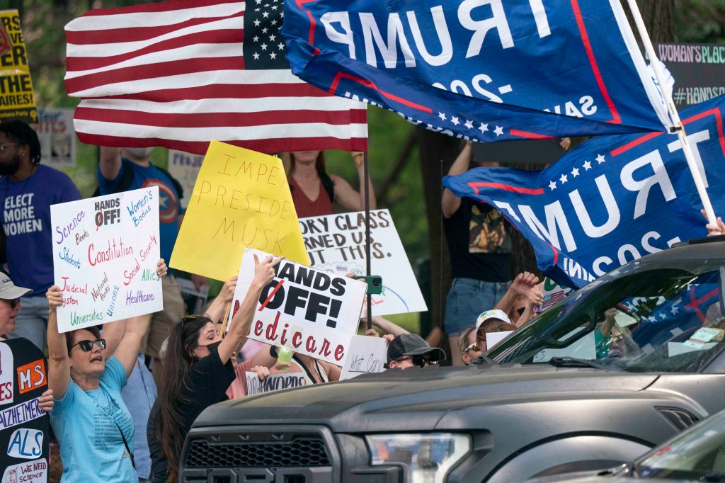 Demonstrators bearing signs while the automobile passes with flags supporting President Donald Trump during a protest at the Statement on April 5, 2025 in Columbia, South Carolina